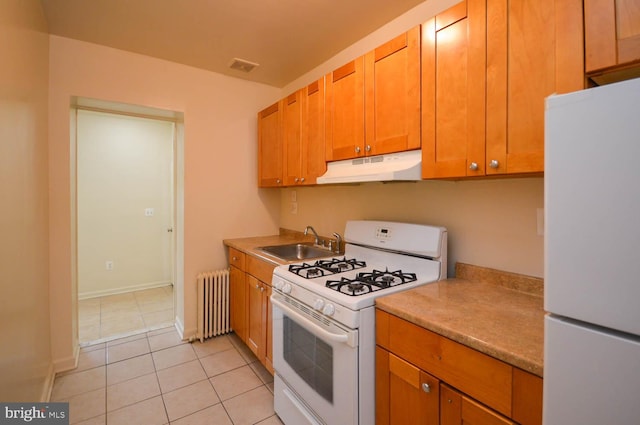 kitchen featuring radiator heating unit, white appliances, light tile patterned floors, and sink