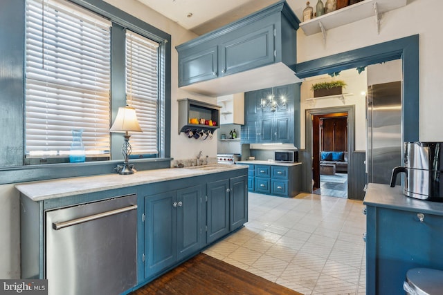 kitchen featuring blue cabinetry, sink, stainless steel appliances, decorative light fixtures, and light wood-type flooring