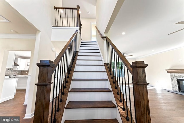 stairway with recessed lighting, crown molding, wood finished floors, and a stone fireplace