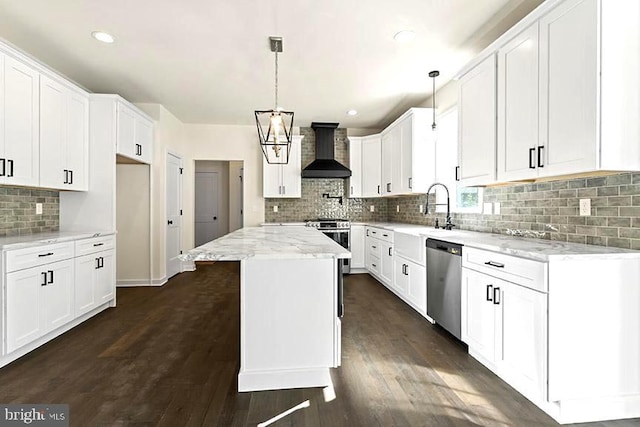 kitchen with appliances with stainless steel finishes, sink, wall chimney range hood, white cabinets, and a center island