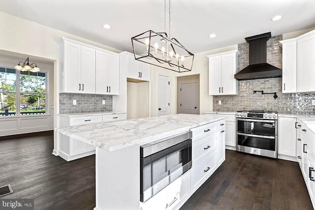 kitchen with built in microwave, wall chimney range hood, a center island, stainless steel stove, and white cabinetry