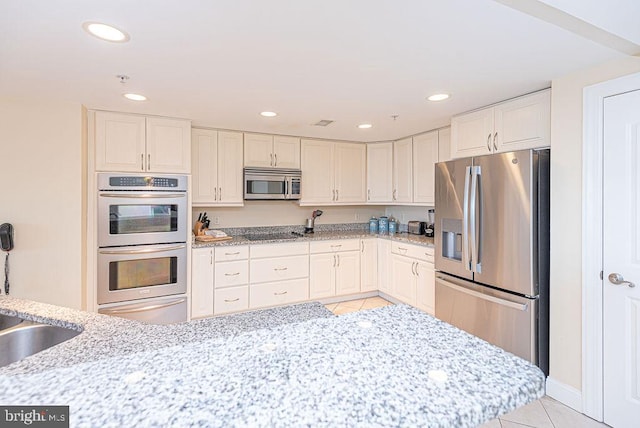 kitchen featuring white cabinets, light tile patterned flooring, light stone countertops, and appliances with stainless steel finishes