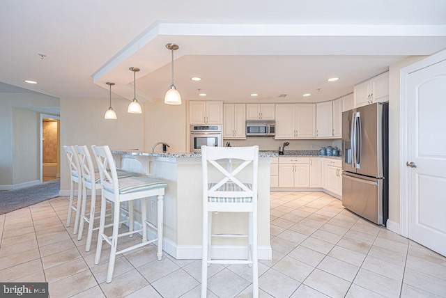 kitchen with a kitchen island with sink, white cabinets, decorative light fixtures, light stone counters, and stainless steel appliances