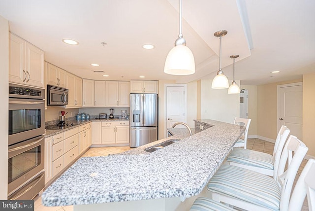 kitchen featuring light stone countertops, stainless steel appliances, sink, decorative light fixtures, and a breakfast bar area