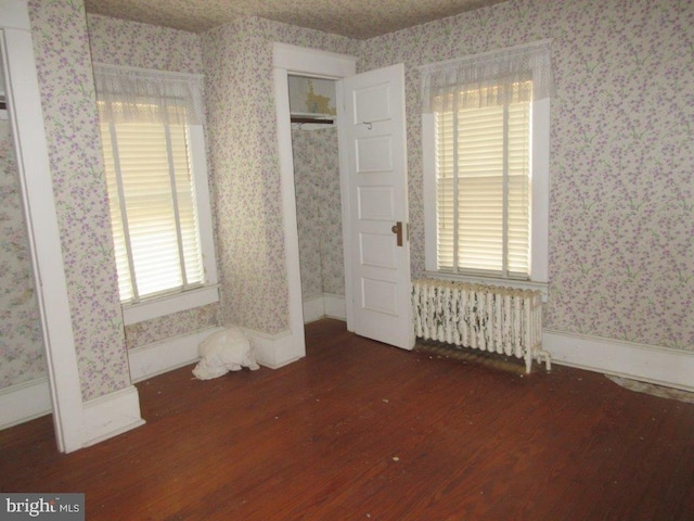 unfurnished bedroom featuring multiple windows, dark hardwood / wood-style floors, and radiator heating unit