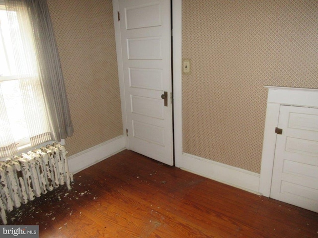 empty room with dark hardwood / wood-style flooring and radiator heating unit