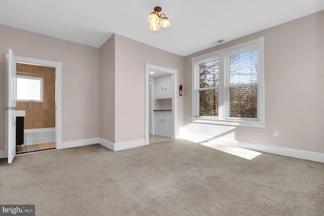 spare room featuring light colored carpet, a wealth of natural light, and a chandelier