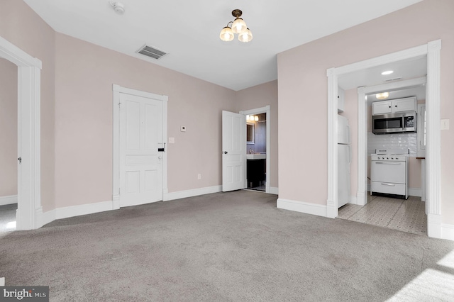 unfurnished bedroom with a chandelier, ensuite bathroom, white fridge, and light colored carpet