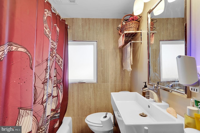 full bathroom with shower / bath combo, toilet, tile walls, and sink