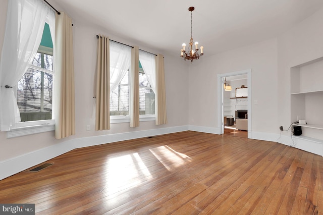 unfurnished dining area featuring hardwood / wood-style floors, built in features, and an inviting chandelier