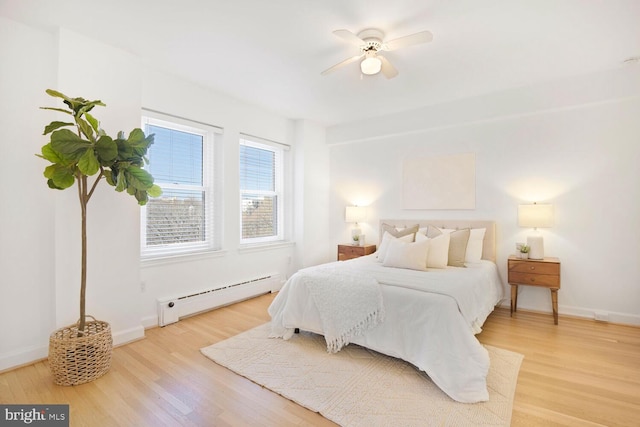 bedroom with a baseboard radiator, light wood-style flooring, and baseboards