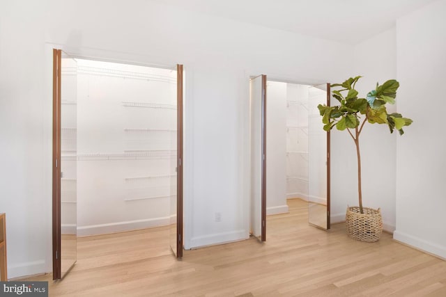 bedroom featuring baseboards, a walk in closet, a closet, and wood finished floors