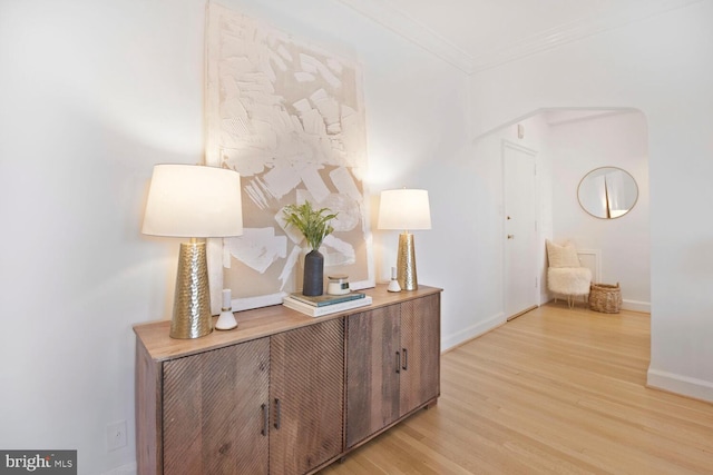 interior space with light wood finished floors, baseboards, arched walkways, and crown molding