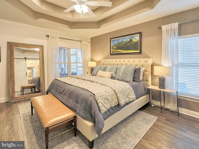 bedroom with hardwood / wood-style flooring, ceiling fan, a barn door, and a tray ceiling