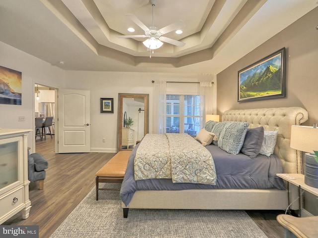 bedroom with dark hardwood / wood-style floors, stainless steel refrigerator, ceiling fan, and a tray ceiling