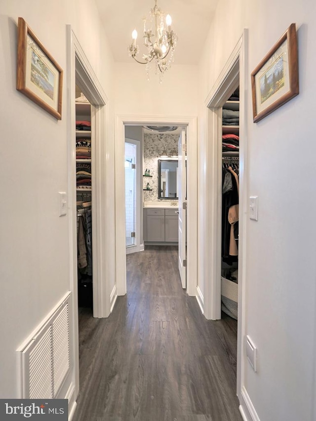 hall with dark wood-type flooring and an inviting chandelier