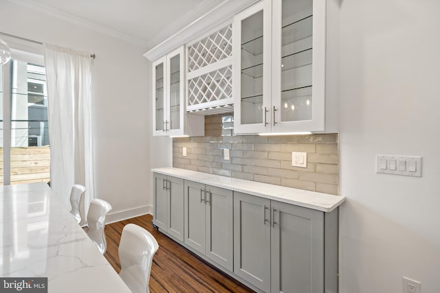 kitchen with gray cabinetry, light stone countertops, dark hardwood / wood-style flooring, decorative backsplash, and ornamental molding