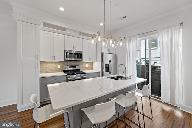 kitchen featuring a center island with sink, a kitchen breakfast bar, sink, decorative light fixtures, and stainless steel appliances