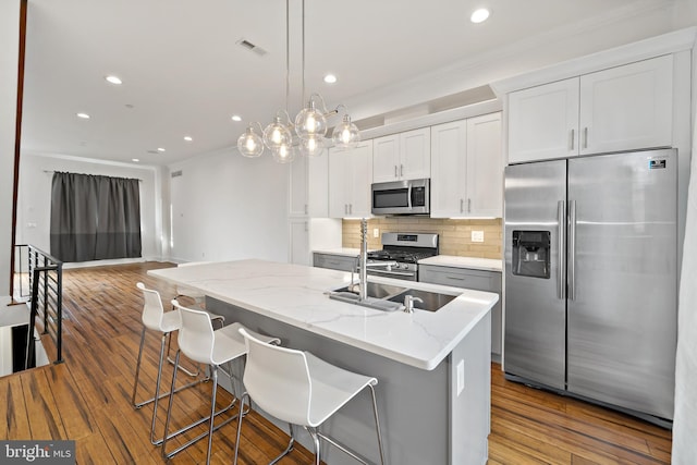 kitchen featuring appliances with stainless steel finishes, a kitchen breakfast bar, a kitchen island with sink, wood-type flooring, and white cabinetry