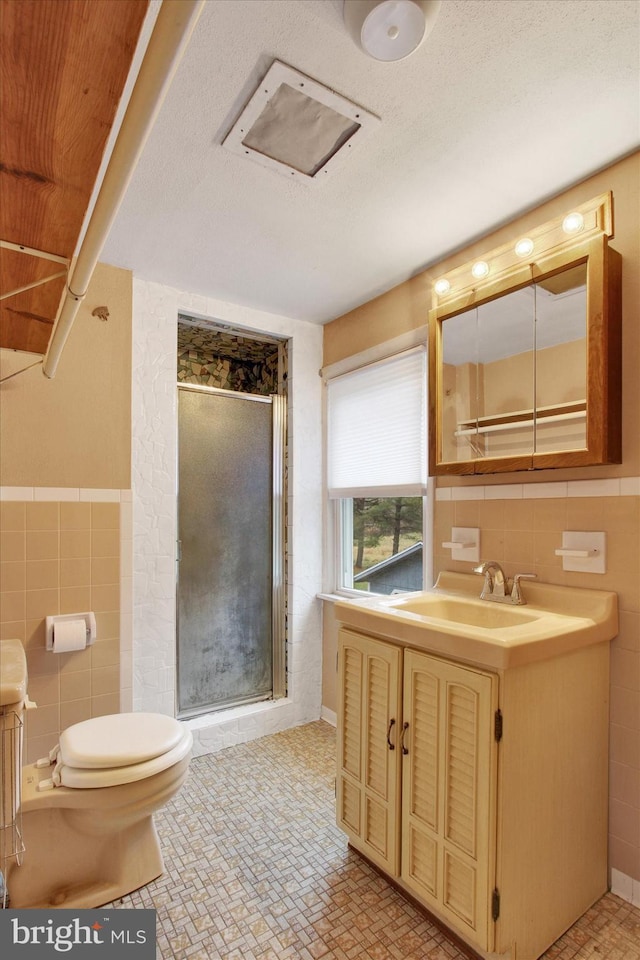 bathroom with vanity, toilet, tile walls, and a shower with shower door