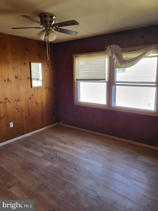 empty room featuring ceiling fan, wooden walls, and wood-type flooring