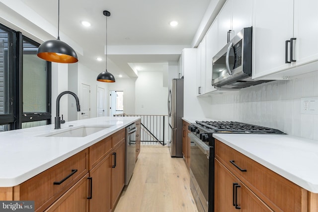 kitchen with appliances with stainless steel finishes, a kitchen island with sink, sink, decorative light fixtures, and white cabinetry