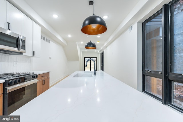 kitchen with light stone countertops, stainless steel appliances, sink, pendant lighting, and white cabinetry