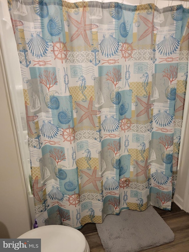 interior space featuring curtained shower, wood-type flooring, and toilet