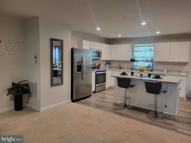 kitchen featuring white cabinetry, a center island, stainless steel appliances, light hardwood / wood-style floors, and a breakfast bar area