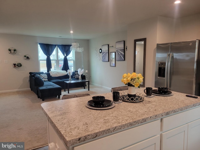 kitchen with a kitchen island, stainless steel fridge with ice dispenser, light stone counters, light carpet, and white cabinets