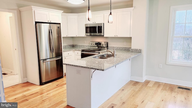 kitchen with pendant lighting, sink, light hardwood / wood-style flooring, appliances with stainless steel finishes, and kitchen peninsula