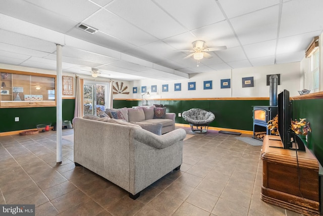 living room featuring tile patterned flooring, a paneled ceiling, a wood stove, and ceiling fan