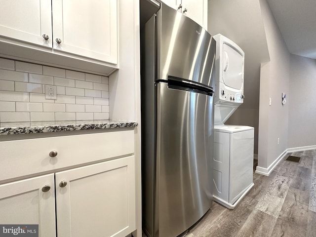 kitchen with stainless steel refrigerator, tasteful backsplash, dark stone countertops, stacked washer / dryer, and hardwood / wood-style floors