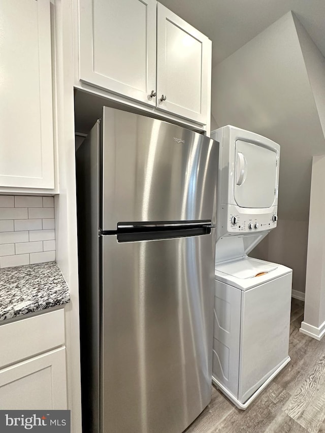 kitchen featuring stainless steel refrigerator, white cabinetry, stacked washer / dryer, and light wood-type flooring