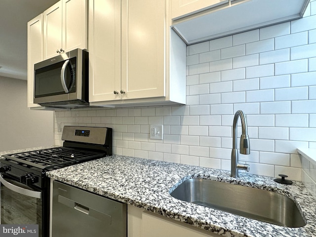 kitchen with light stone countertops, white cabinetry, sink, stainless steel appliances, and decorative backsplash