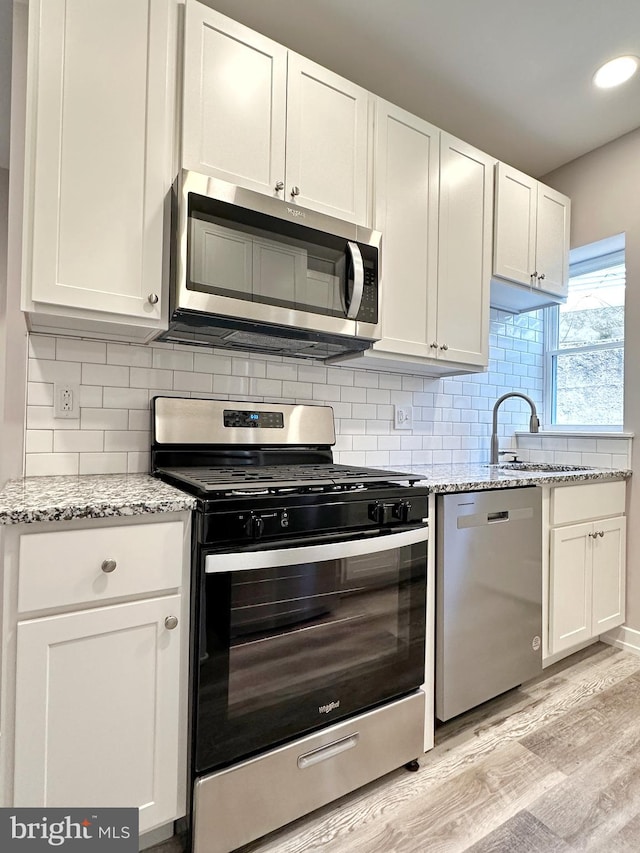 kitchen featuring light stone countertops, light hardwood / wood-style flooring, decorative backsplash, white cabinets, and appliances with stainless steel finishes