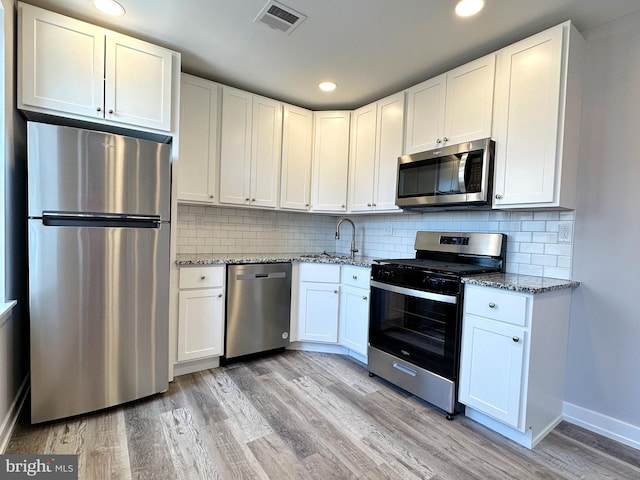 kitchen with white cabinetry, tasteful backsplash, light stone counters, light hardwood / wood-style flooring, and appliances with stainless steel finishes