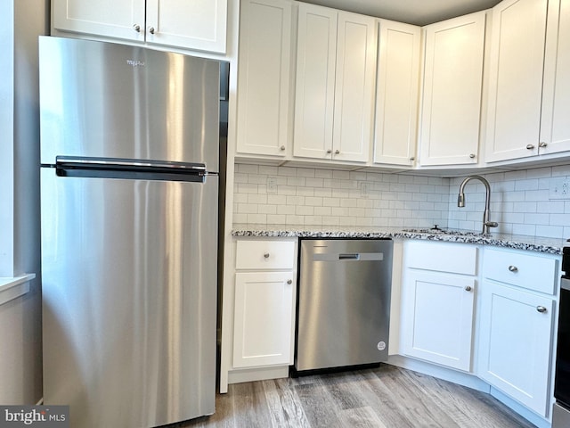 kitchen with decorative backsplash, stainless steel appliances, white cabinetry, and light hardwood / wood-style flooring