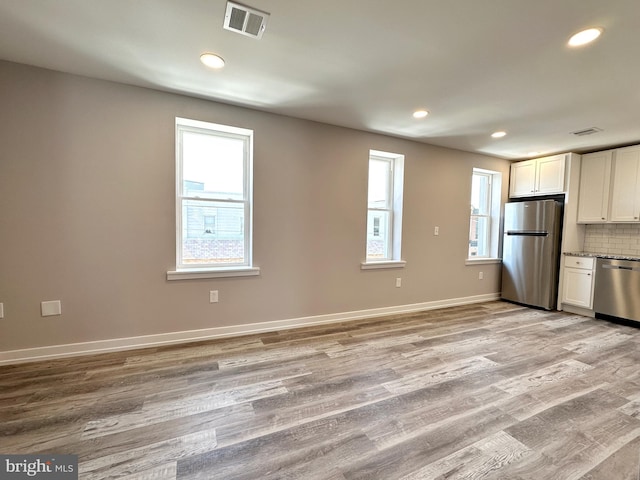 kitchen with white cabinets, light hardwood / wood-style floors, backsplash, and appliances with stainless steel finishes