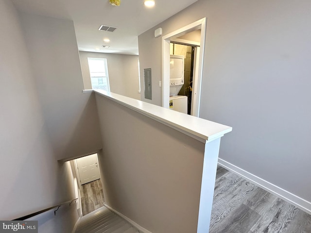 staircase featuring wood-type flooring, electric panel, and stacked washer / drying machine