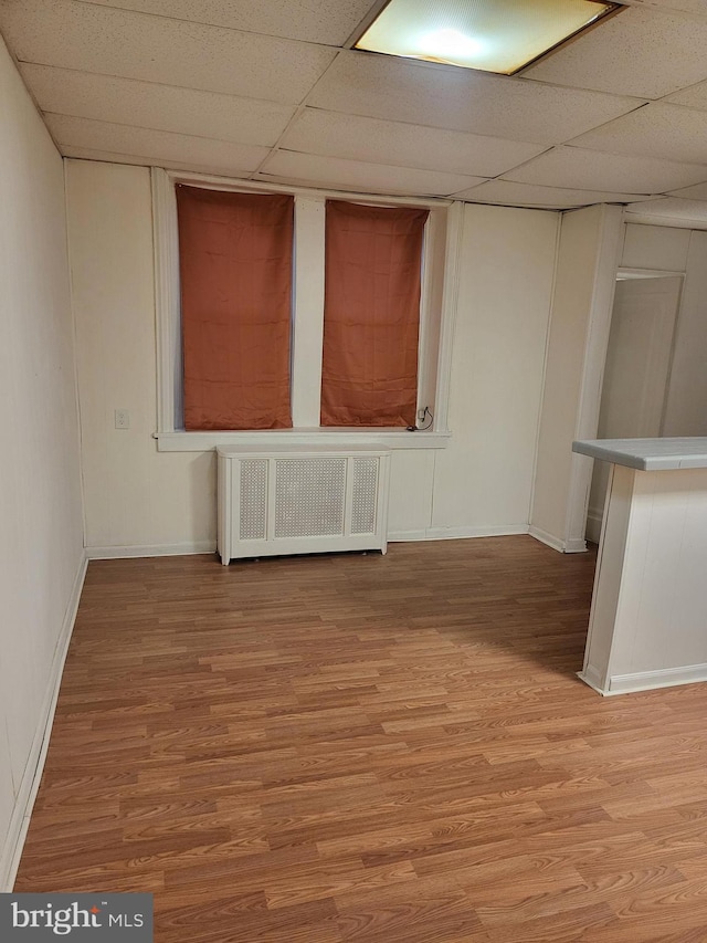 spare room featuring radiator, a paneled ceiling, light hardwood / wood-style flooring, and bar area