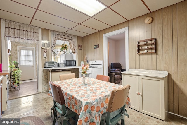 dining space with a paneled ceiling, wooden walls, and washer / dryer