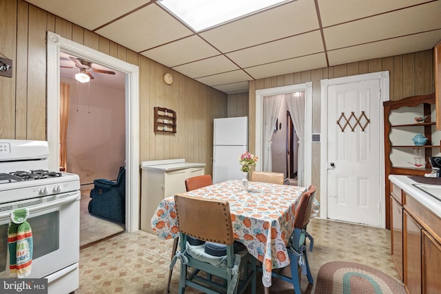 kitchen featuring a paneled ceiling, ceiling fan, white appliances, and wooden walls