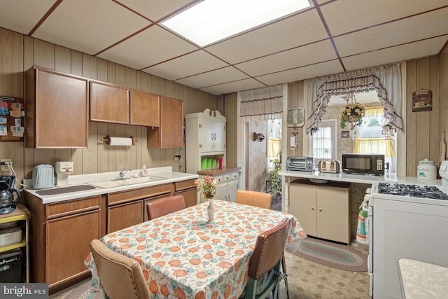 kitchen featuring a paneled ceiling, white gas range oven, wooden walls, and sink