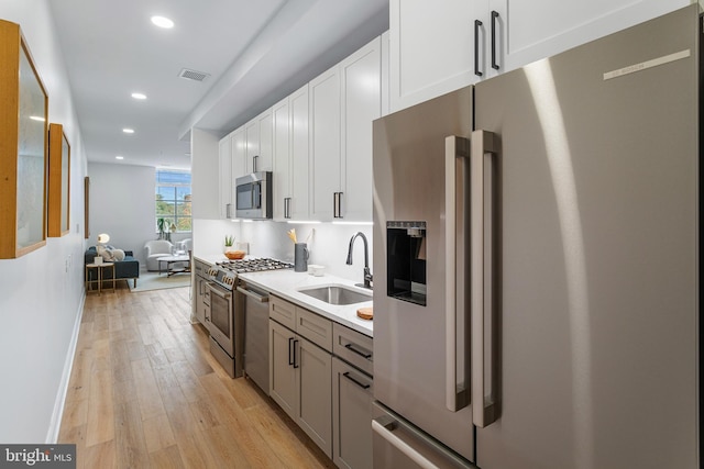 kitchen with premium appliances, light hardwood / wood-style floors, white cabinetry, and sink