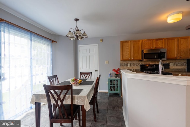 kitchen featuring pendant lighting, dark tile patterned flooring, black range, tasteful backsplash, and a notable chandelier