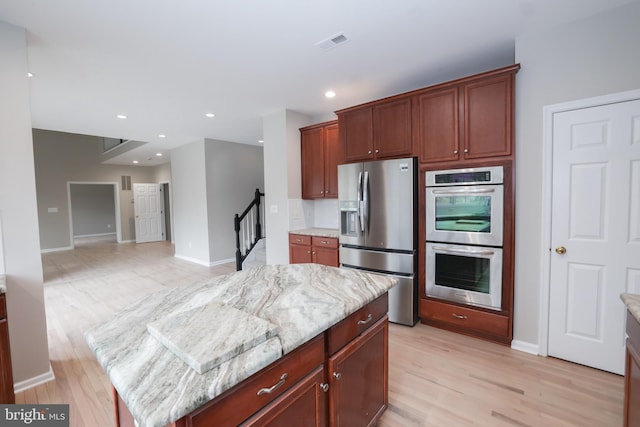 kitchen featuring stainless steel appliances, a kitchen island, light hardwood / wood-style floors, and light stone counters