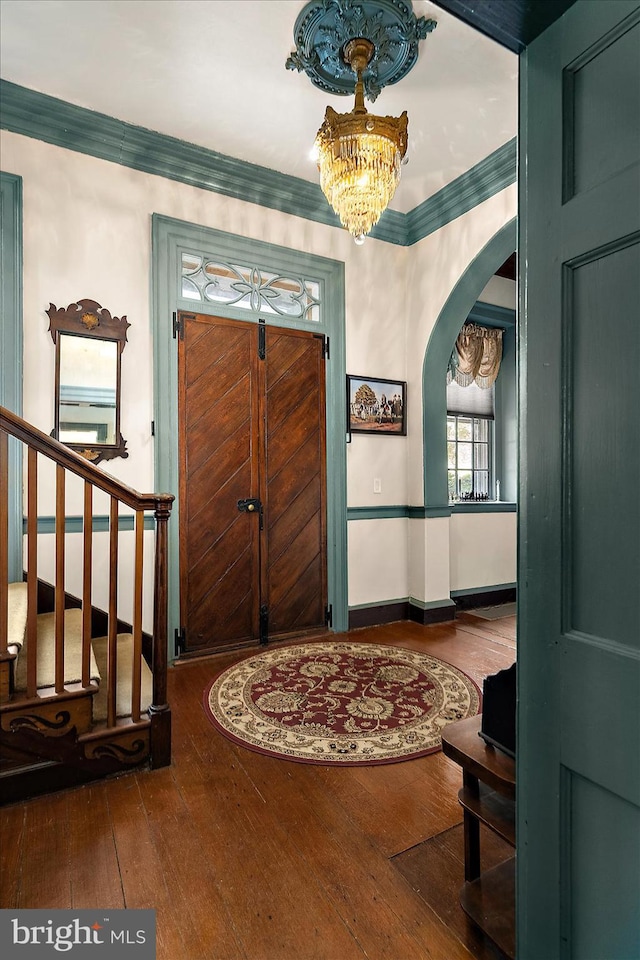 entryway with a notable chandelier, wood-type flooring, and crown molding