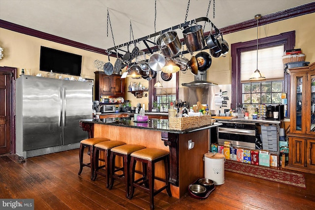 kitchen featuring dark wood-type flooring, appliances with stainless steel finishes, a breakfast bar, a kitchen island, and ornamental molding