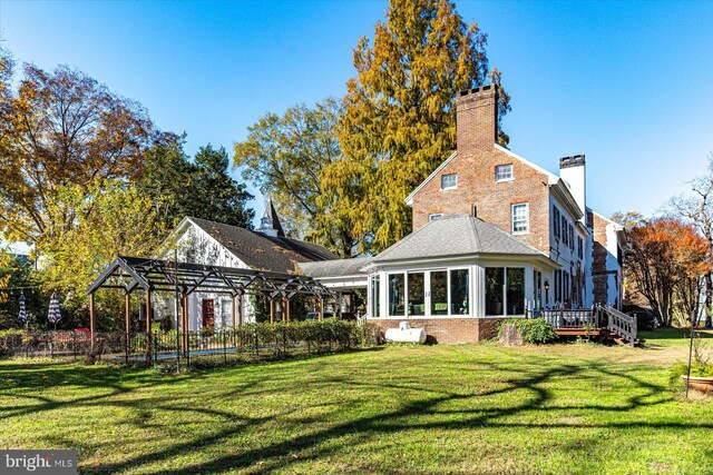 back of house with a sunroom, a deck, and a lawn